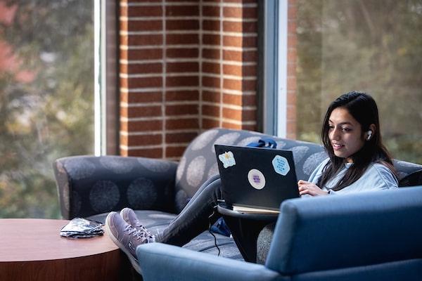 A 博彩网址大全 student works on her laptop while sitting on a couch in Pius XII Memorial Library.